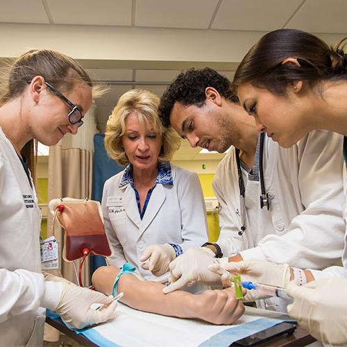 Nursing students learning how to inject blood into a practice arm